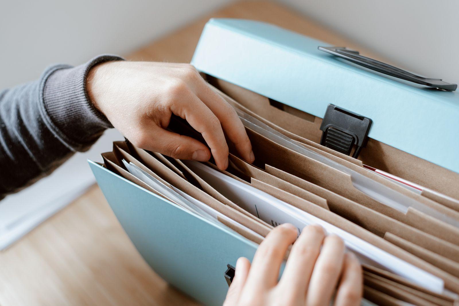 Hands lifting a sheet from the dividers of an expanding document file on a desk
