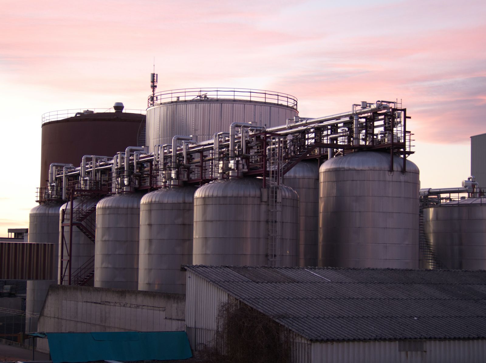 Storage tanks linked by an elevated pipe rack at an industrial processing site