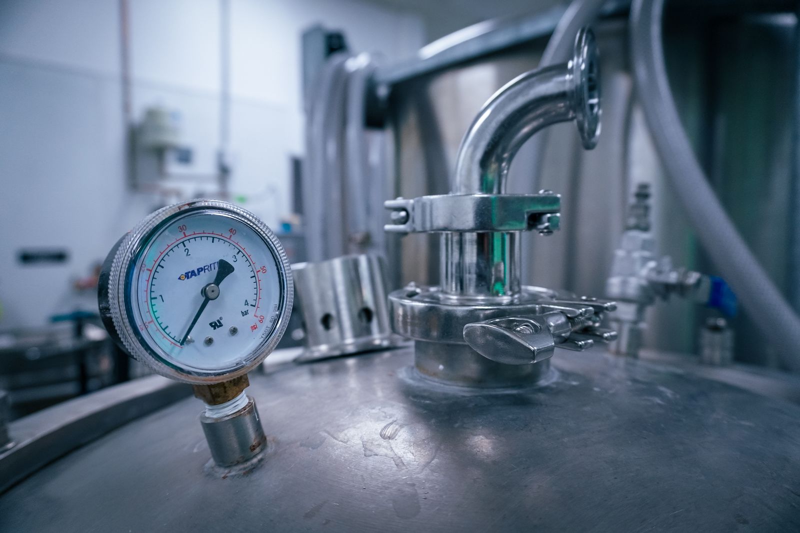 A pressure gauge and clamped fitting on the head of a stainless steel vessel