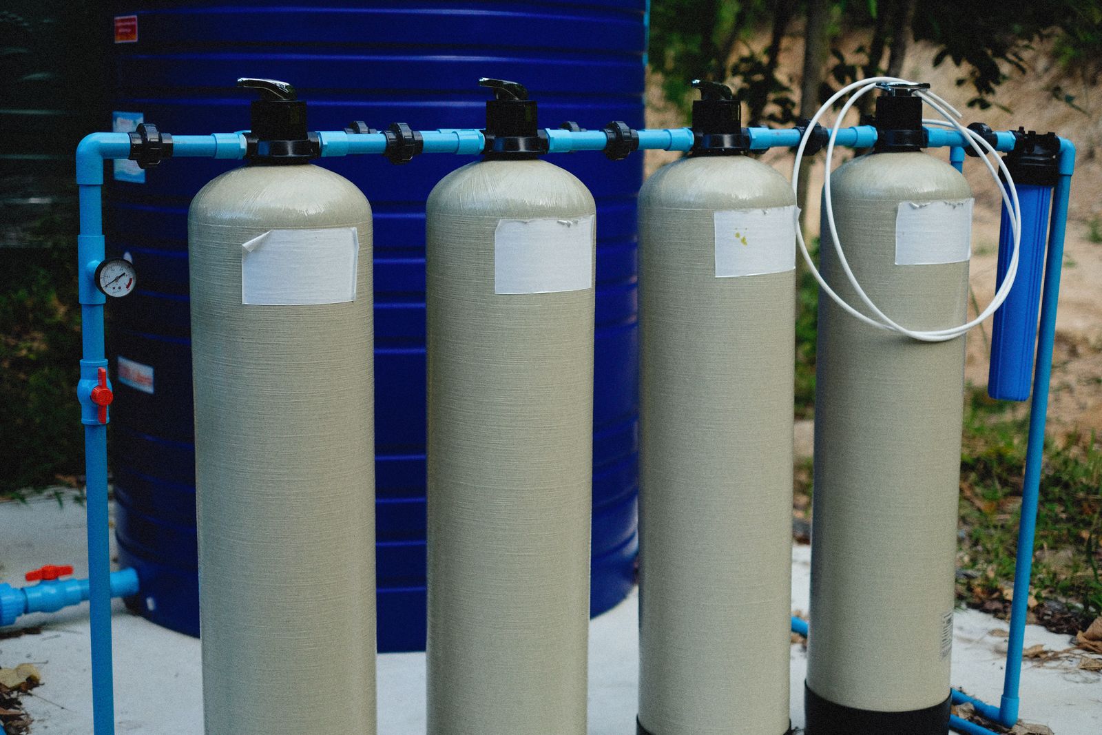 A row of fibreglass pressure vessels plumbed into a common manifold with a pressure gauge, beside a bulk water tank